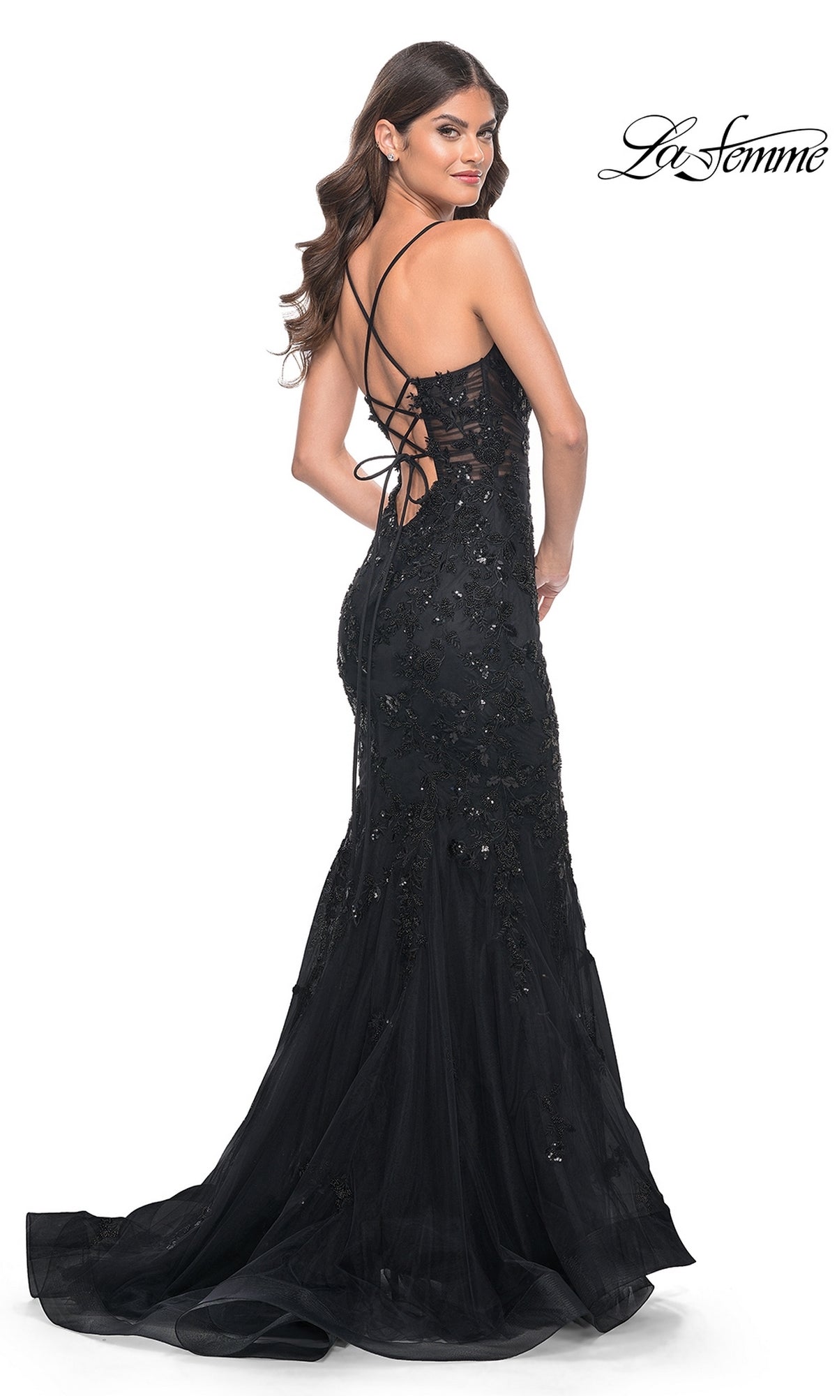 A woman poses in the La Femme Tonal Lace Long Mermaid Prom Dress 32033, featuring black beaded lace and an open lace-up back, with her head turned over her shoulder. The